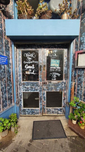 Glass doors with blue frames ahead. Push in centre to open.