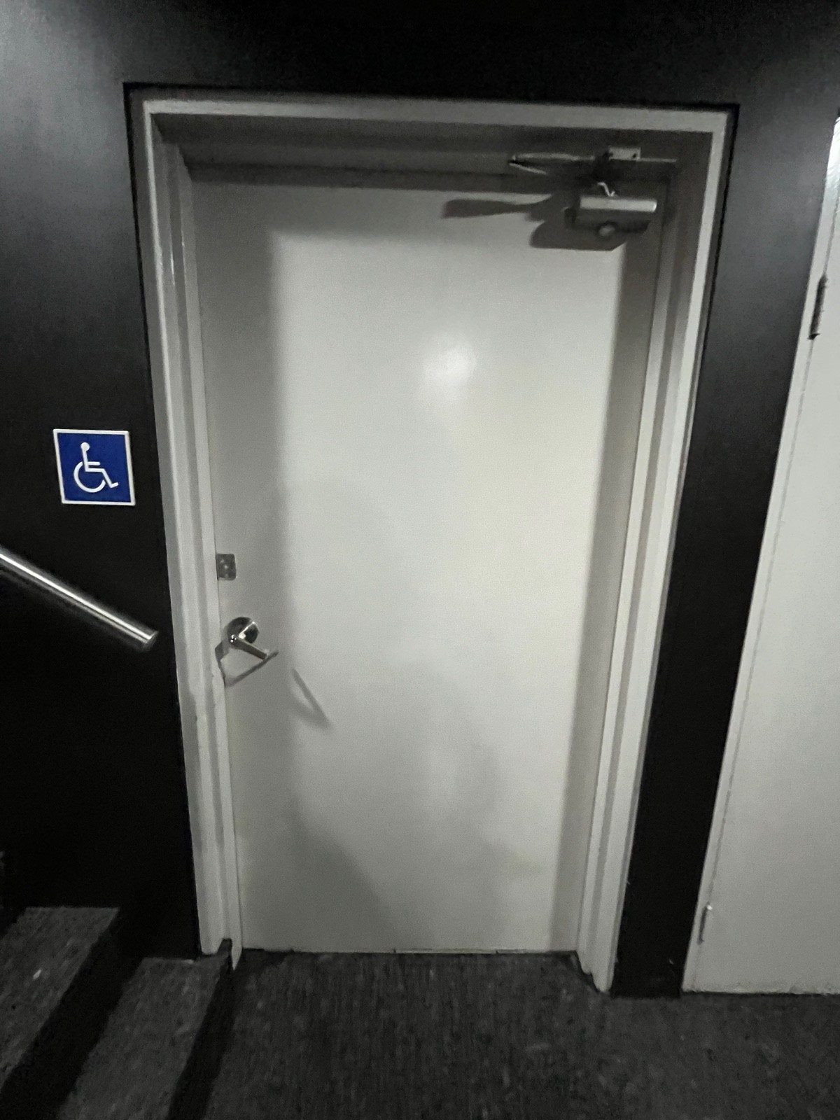 From after ramp facing straight. White wooden bathroom door. Insert key and turn right. Turn silver handle and push from left.
