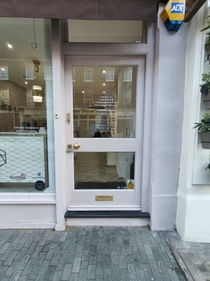 Glass door in pink wooden frame. Push golden metal handle on left to open. Doorbell on left of door.