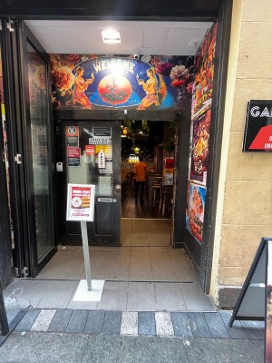 Glass doors with black metal frame fold open to left. Folding door followed by glass double doors. Push from middle. Signage obstructing on left.