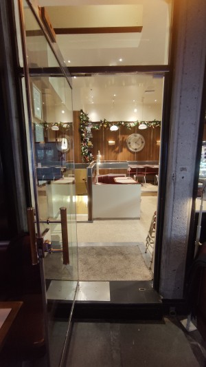 From back of outdoor area facing straight. Glass door ahead. Pull brass handle on right to open.