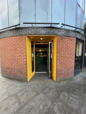 Black metal-framed glass door. Yellow walls surrounding door. Pull silver handle on left to open.