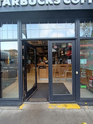 Glass doors with black frame. Push silver, metal handle on middle to open. Doorbell for assistance on right of door.