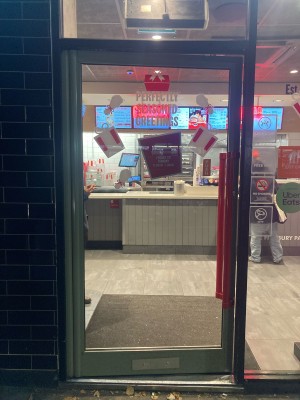 Glass door with metal frame ahead. Push to open via red hand rail on right.