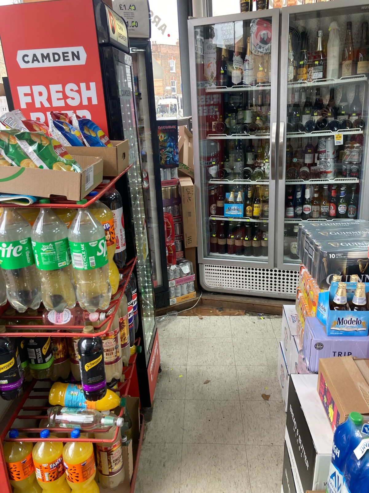 From entrance, facing left. Path ahead with product shelves on both sides. Fridges on back left and back.