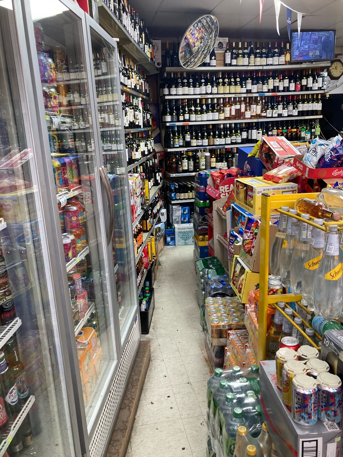 From fridges, facing right. Path ahead with fridges along left. Product shelves along back left, back and along right.