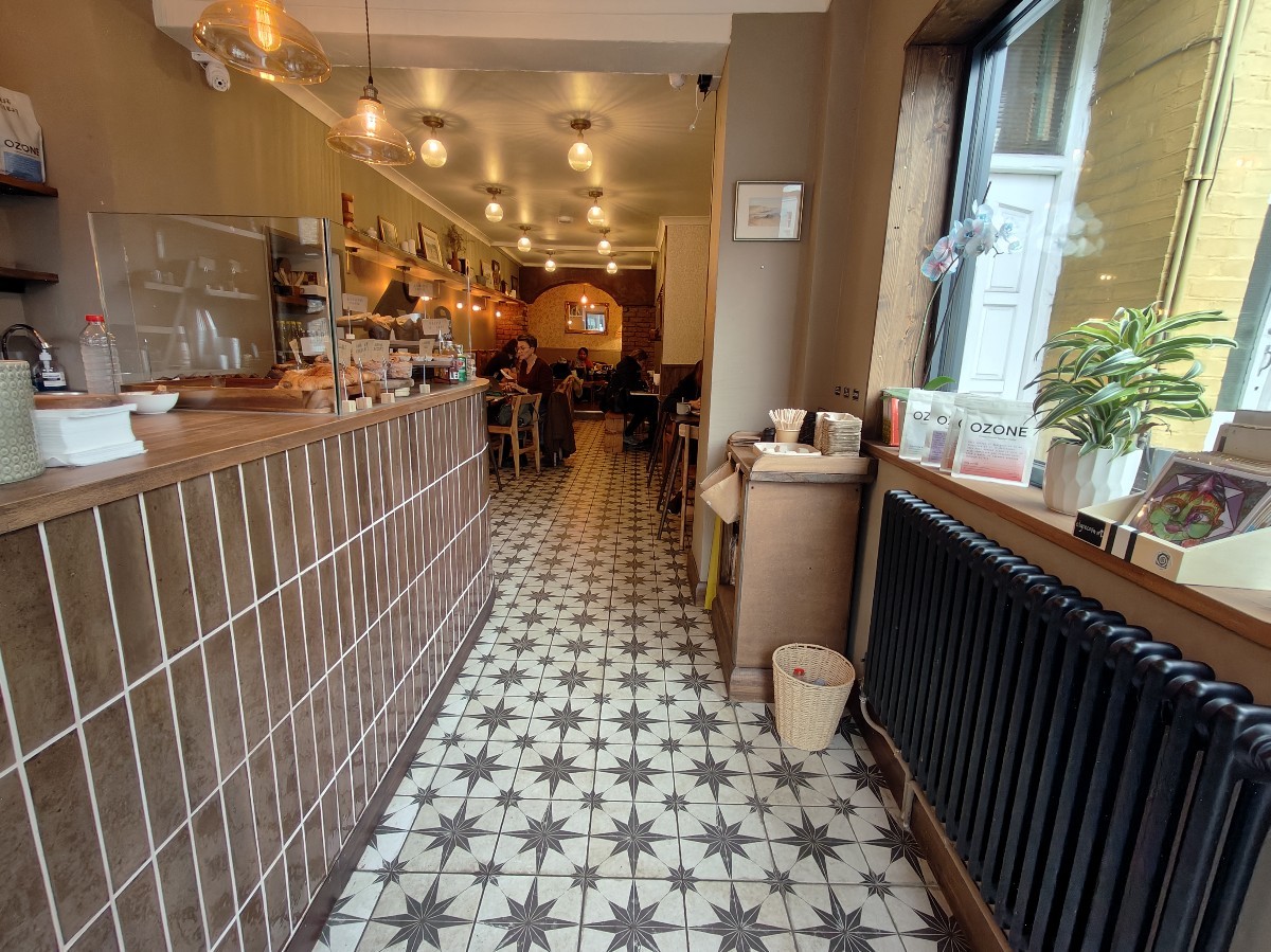From entrance facing right. Product shelf on right. Condiment station at back right. Path ahead to seating. Display counter and till on left.