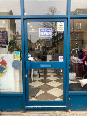 Glass door with blue frame ahead. Push to open via blue handle on left.