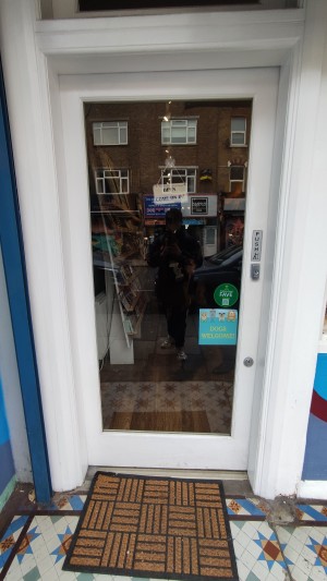 Glass door with white frames. Push on right to open.