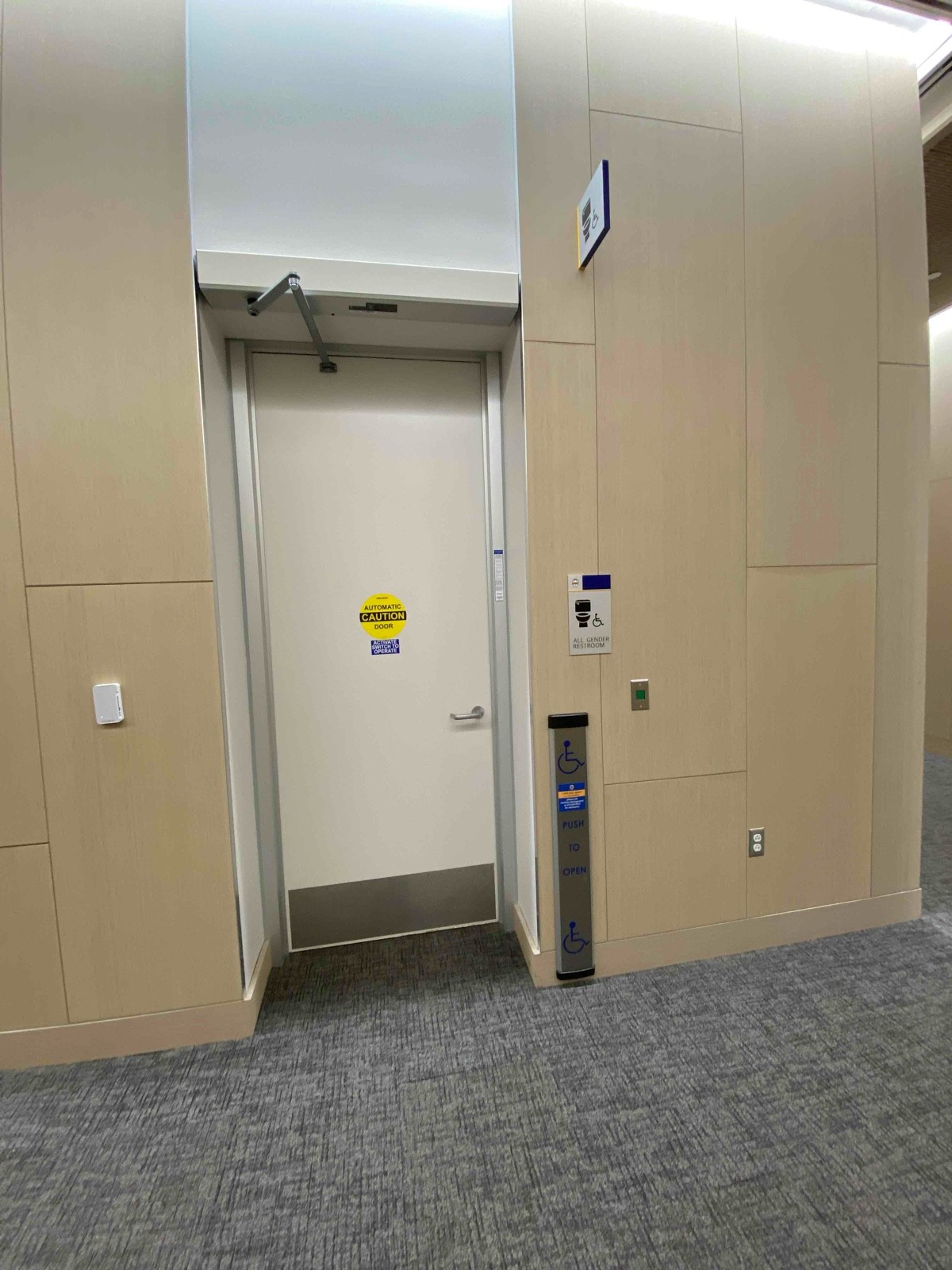 Long, low-to-ground push button for automatic door, pull-door, all-gender restroom, no obstruction to bathroom unless people in line for elevator
