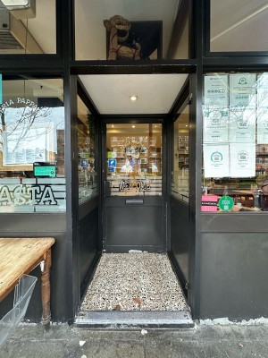 Opening ahead, followed by black metal and glass panelled door. Metal handle on left, push to open.