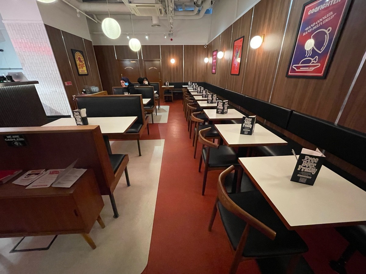 From round table facing left. Welcome desk followed by booths along left. Half booths with chairs along right and far back.