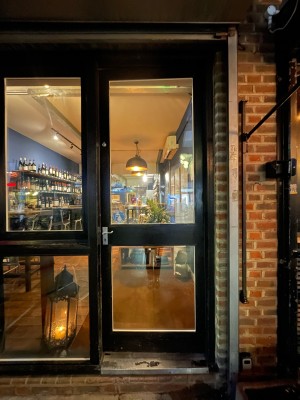 Glass door with black frame. Push metal handle on left to open.