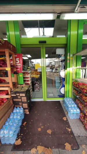 From pavement facing venue. Built in ramp ahead with doormat. Glass automatic doors with green frames at the back.