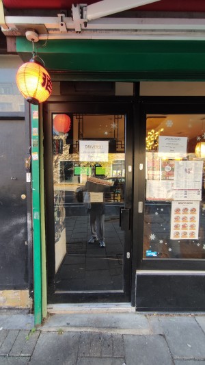 Glass door with black frame. Push metal handle on right to open. One step up at foot of door. Archway to right after door.