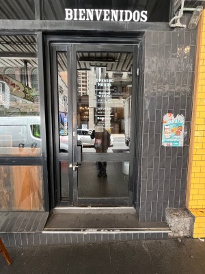 Glass door with black metal frame. Push black metal handle on left to open.
