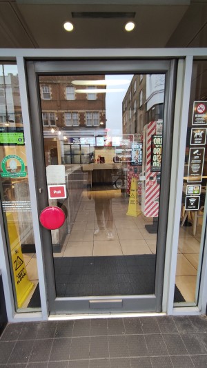 Glass door with grey frames. Pull red handle on left to open.