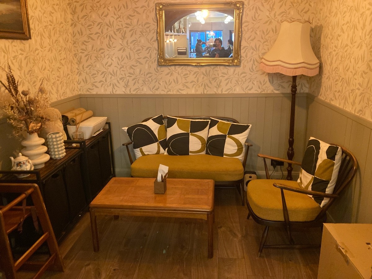 From archway, facing straight. Baby chair on left, shelve behind. Low table ahead, couch behind. Armchair on right.