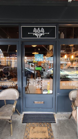 Glass door with grey frame. Push metal handle on left to open.