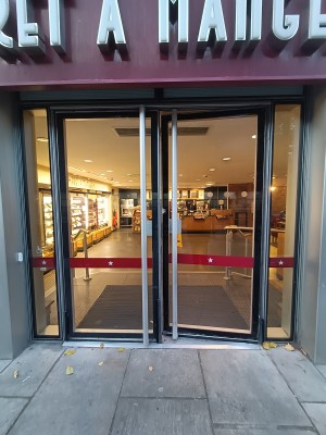 Glass doors with black frames. Push silver, metal handles in middle to open. Doorbell on left of doors.