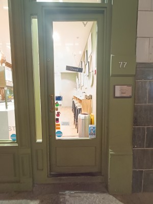 Glass door with green frame. Push golden metal handle on left to open.
