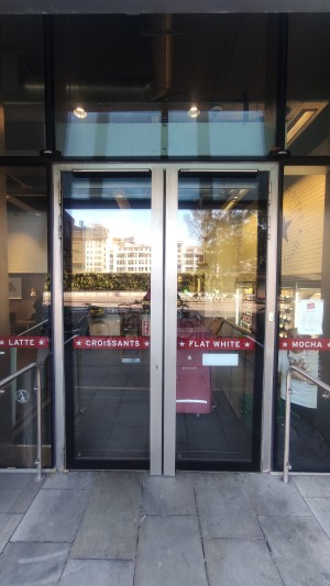 Glass doors with grey frames ahead. Pull metal handles in centre to open.