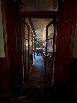 From left of side area of The King’s Arms, facing left. Wood-framed glass door ahead. Push from brass handle at centre to open.