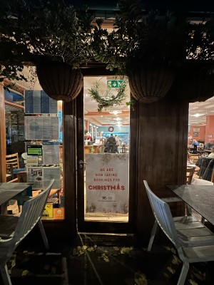 Glass door with wooden frame. Push metal handle on left to open. Tables and chairs to left and right.