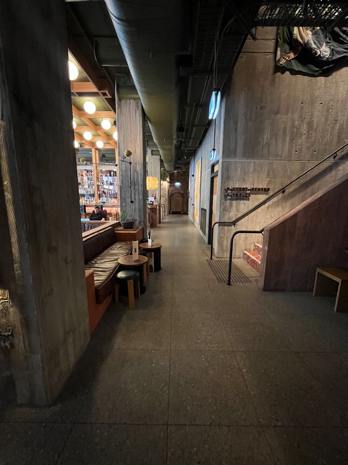 From staff desk facing left. Half booths with low table and stools on left. Path to side area ahead. Desk on right followed by path to back area.