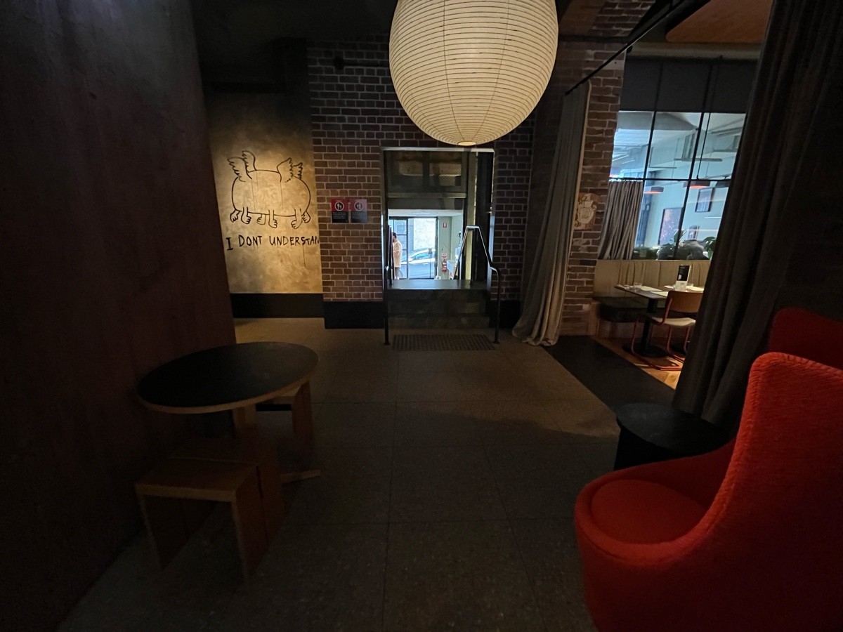 From after tables and stools facing straight. Tables and stools on left. Low table and armchair on right. Path to bathroom facing left ahead.