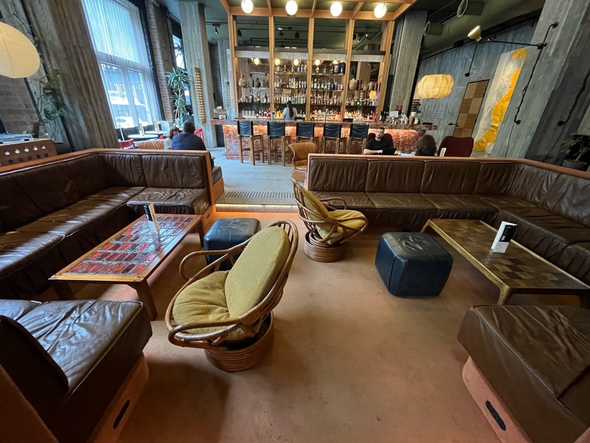 From step facing straight. Half booths along left and right with low tables, stools, and armchairs.