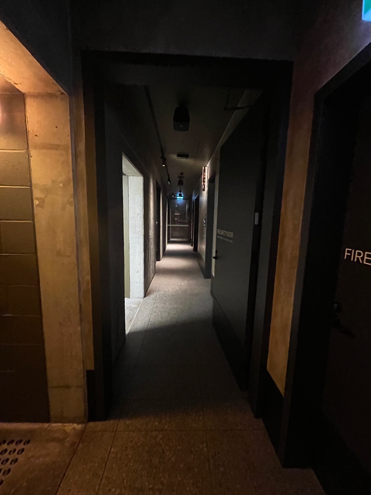 From end of hallway facing straight. Black wooden preceding door. Turn black handle and push from left.