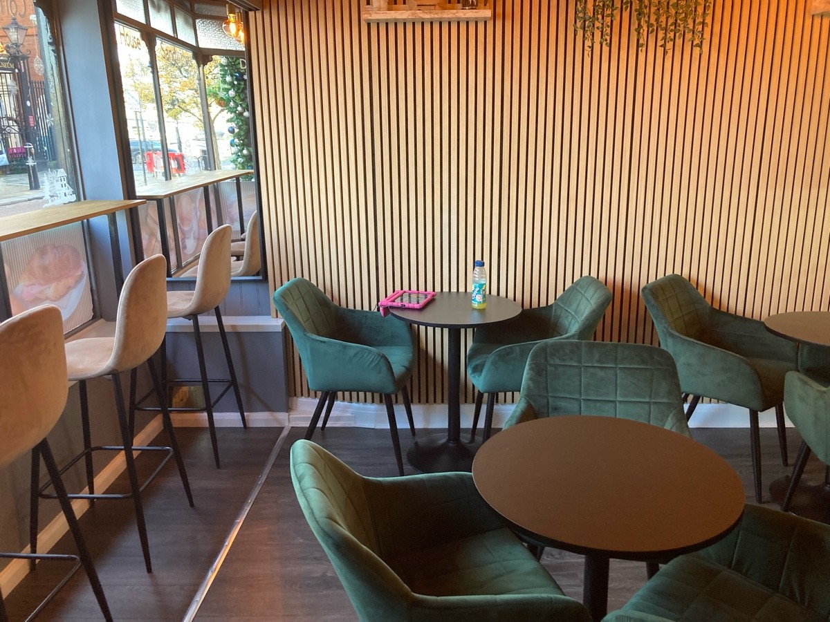 From entrance, facing left. High table and stools along left. Tables and chairs ahead, and along back wall.