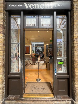 Black framed glass doors. Push from centre to open. Assistance doorbell right of door.