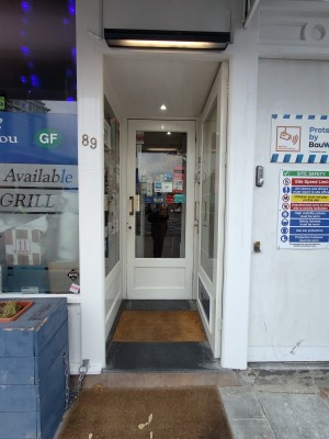 Facing first preceding door. White framed glass door. Push golden handle on left to open.