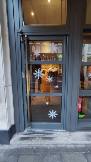From pavement facing venue. Glass door with grey frames ahead. Pull wooden handle on left to open.