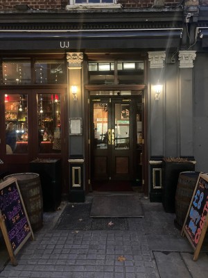 From street, facing venue. Path ahead to first set of doors on back. Barrels and A-framed signs along left and right.