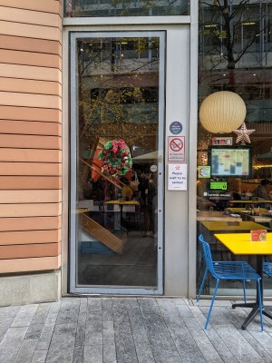 From pavement facing straight. Glass door without handle. Push from right to open.