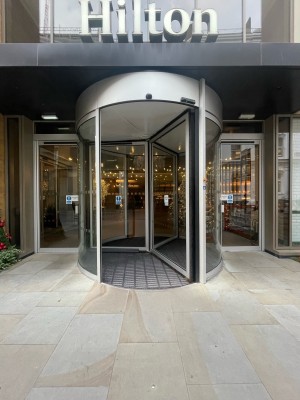 From street facing venue. Revolving doors ahead. Accessible entrance to its left.
