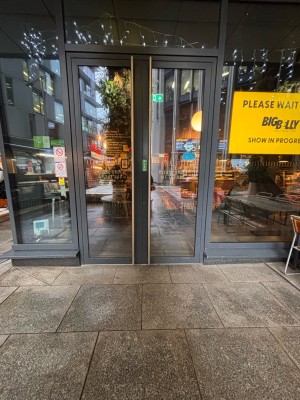 Facing glass doors with grey wooden frame ahead. Pull metal handles at center to open.