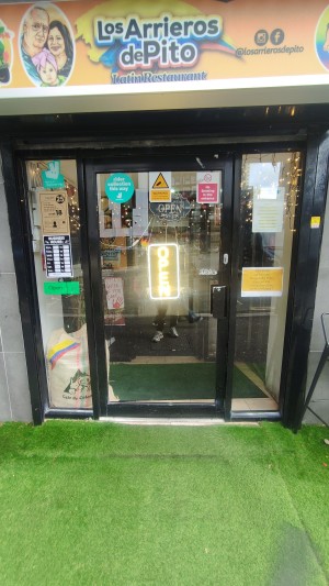 Glass door with black frames ahead. Push black handle on right to open. Artificial grass before door.