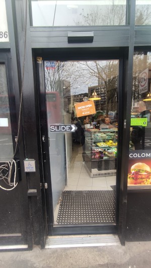 Glass door with black frame ahead. Slide black handle from left to right to open or press button on left to open.