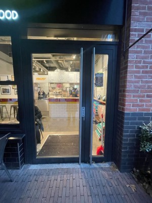 Glass door with black frame ahead. Push door to open via handrail on right.