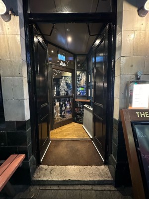 Black wooden doors. Push from centre to open. A-frame sign on right. Picnic bench on left.
