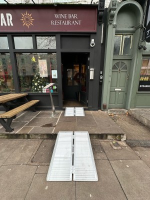 From pavement facing venue. One step up. Outdoor seating to left.