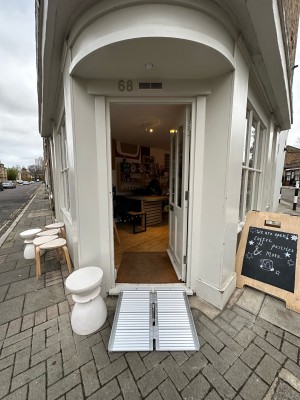 White and glass panelled door. Push metal handle on left to open. A-frame sign on right. Stool on left.