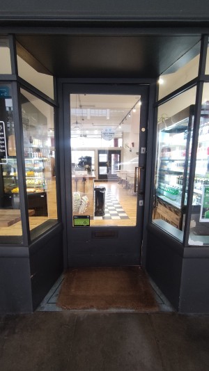 Glass door with grey frames. Push brass handle on right to open. Glass walls to left and right of entrance.