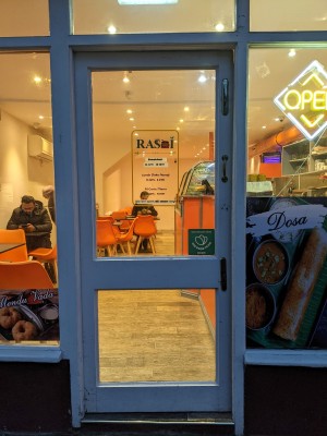 Glass door with white wooden frame. Metal handle on right, push to open.
