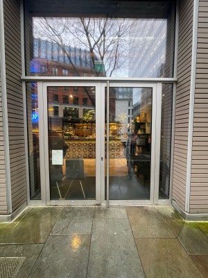 Glass door with grey frame. Push on metal handle in middle to open.