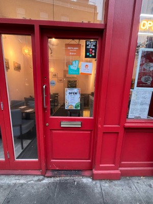 Glass paneled door with red wooden frame ahead. Push metal handle at left to open.
